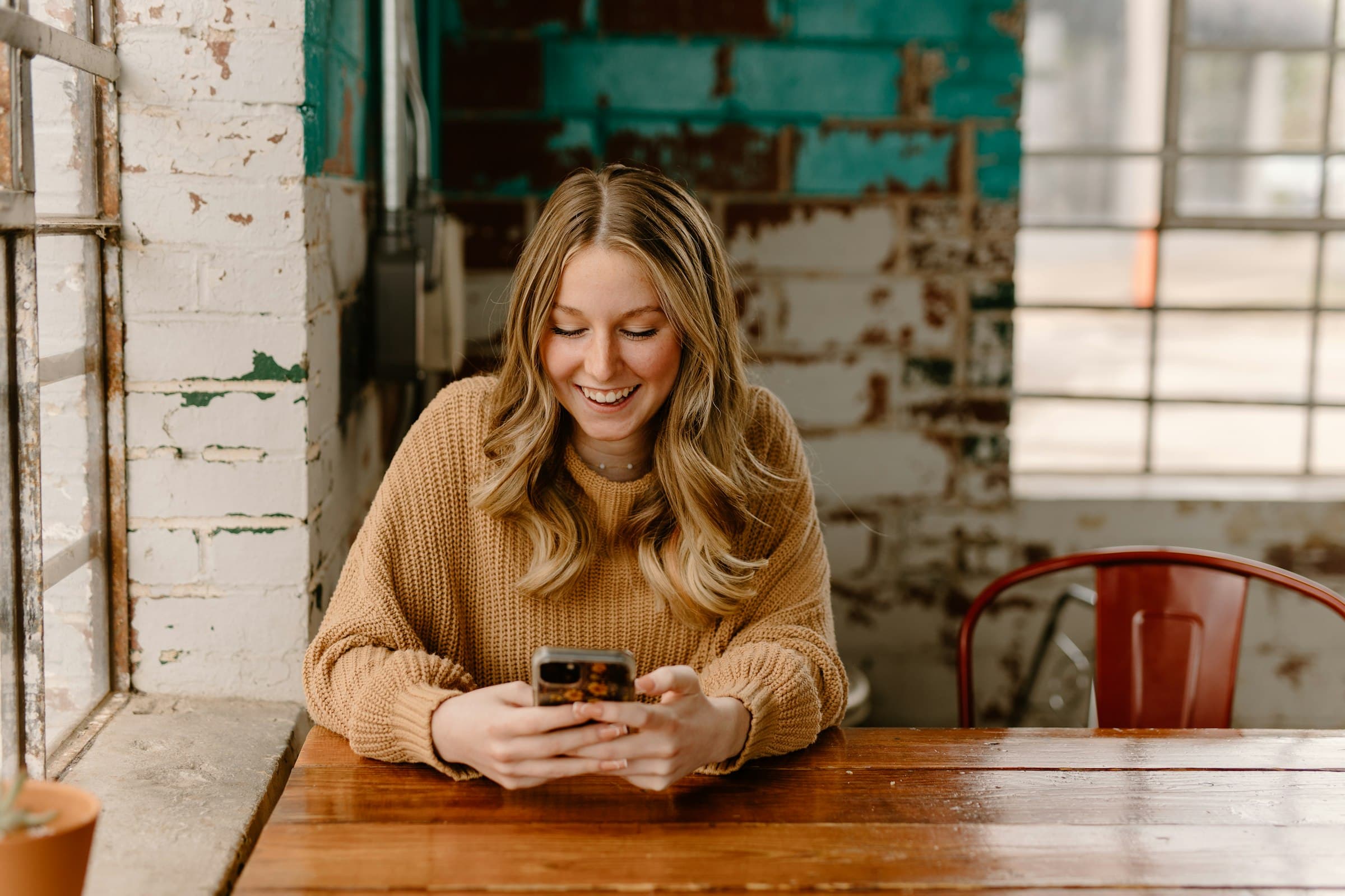 A customer smiles at a text message on her phone at a cafe table